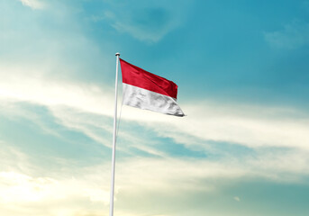 Monaco flag is waving on a tall flagpole among the clouds. Monaco national flag for independence day.