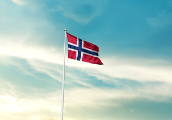 Norway flag is waving on a tall flagpole among the clouds. Norway national flag for independence day.