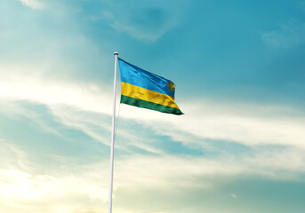 Rwanda flag is waving on a tall flagpole among the clouds. Rwanda national flag for independence day.