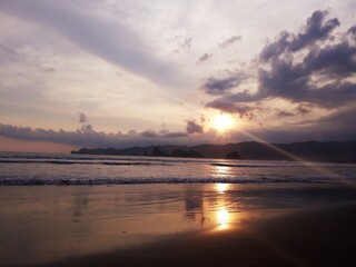 Golden sunlight bathes the sky and water, reflecting a beautiful sunset or sunrise over the beach horizon