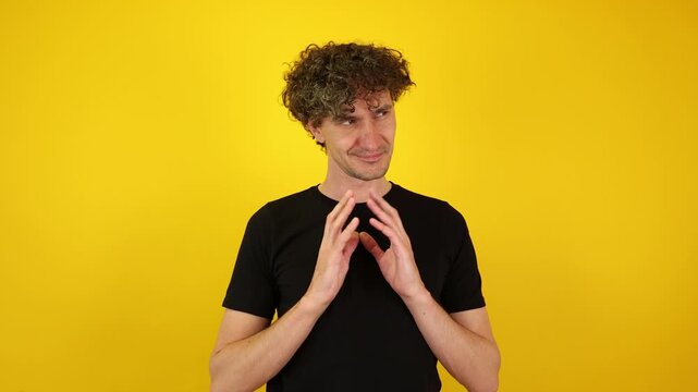 Scheming man with a wicked grin rubs his hands together against a yellow studio backdrop. Ideal for Halloween promos, villain-themed campaigns, and dark humor content.