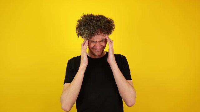 A man sits isolated against a yellow studio background, rubbing his temples in visible discomfort. Ideal for burnout awareness, mental health campaigns, and World Mental Health Day visuals.