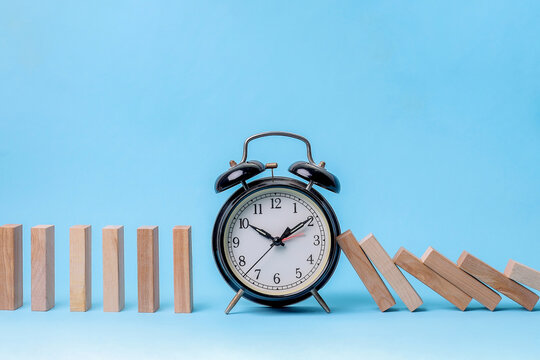 Black Alarm Clock Blocks Falling Dominoes, Symbolizing Timing Interruption - Powered by Adobe