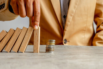 Finger Stops Falling Dominoes Just Before They Hit Coin Stack, Symbolizing Financial Protection