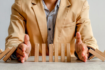 Businessman Uses Both Hands To Stop Falling Dominoes