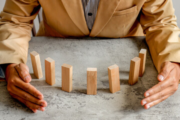 Businessman In Working Clothes Protecting Wooden Dominoes From Falling, Symbolizing Risk Prevention