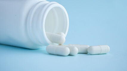 medicine pills capsule spilling out of bottle on blue background