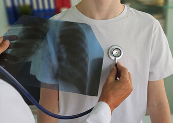 Doctor examines patient using stethoscope while reviewing X-ray