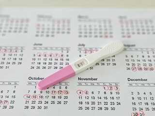 Pregnancy test kit placed on marked calendar highlighting ovulation or menstrual tracking dates concept