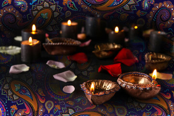 Diya lamps for Diwali, candles and flower petals on dark background