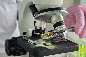 The scientist used tweezers to place a fish oil pill on the microscope specimen tray and prepare for research. Research scientific products, medicinal products, fish oil, omega or vitamins concept