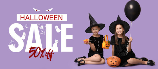 Cute little girls dressed for Halloween as witches with pumpkins, balloon, bag and candies sitting on purple background