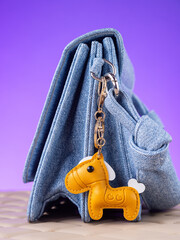 Close-up of a yellow leather bag charm in the shape of a cute pony with a saddle on blue bag