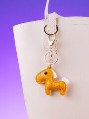 Close-up of a yellow leather bag charm in the shape of a cute pony with a saddle on white bag
