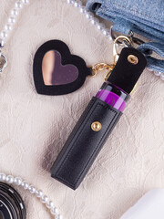 Close-up of a black  leather lipstick case with a heart-shaped mirror, elegantly placed on a lace...