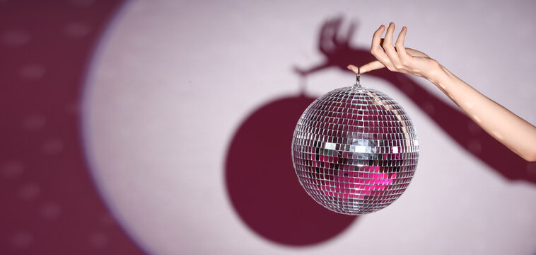 Female hand with disco ball on color background