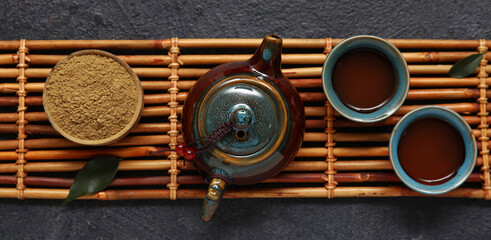 Bamboo tray with cups of refreshment matcha tea and ceramic teapot on black background