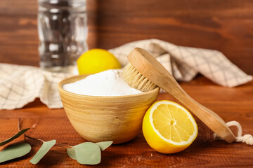 Bowl of baking soda, cleaning brush and lemon on wooden background