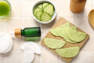 Cotton under-eye patches made with cucumber and materials on light tile background