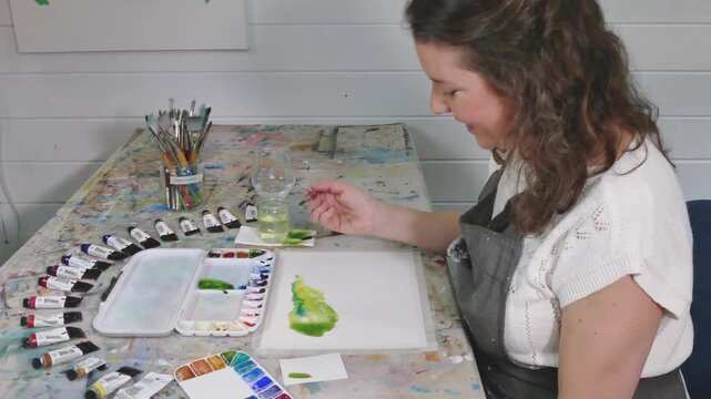 Watercolor painter painting water onto paper, seen from the side, making color swatches