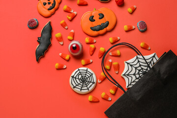 Shopping bag with tasty candy corns and cookies for Halloween on red background