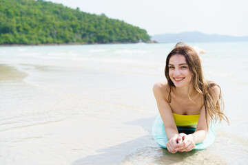 Smiling woman poses with surfboard on a bright beach day.