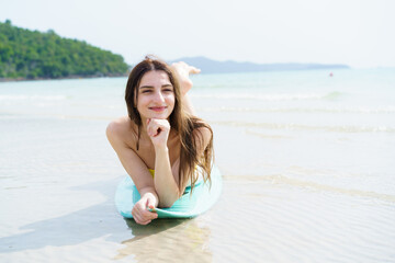 Smiling woman poses with surfboard on a bright beach day.
