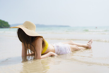 Woman lies on beach sand with soft waves on a sunny summer day.