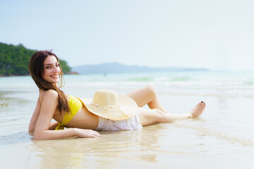 Woman lies on beach sand with soft waves on a sunny summer day.