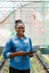 Female African farmer checks vegetables in a greenhouse and records data on her tablet.