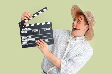 Handsome young man dressed for Halloween as scarecrow with clapperboard on green background