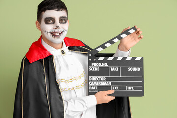 Handsome young man dressed for Halloween as vampire with clapperboard on green background