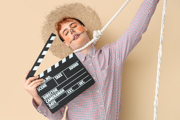 Young man dressed for Halloween as scarecrow with clapperboard and rope on beige background