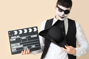 Handsome young man dressed for Halloween as pirate with clapperboard on beige background