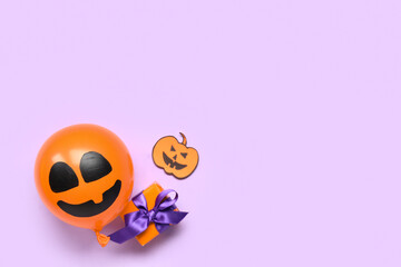 Funny Halloween orange balloon with gift box and paper pumpkin on lilac background