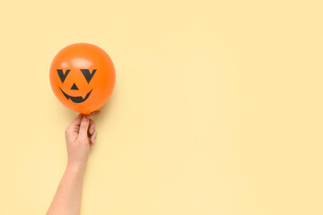 Female hand with funny Halloween orange balloon on yellow background