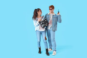 Scary young couple dressed for Halloween as zombies with movie clapper on blue background