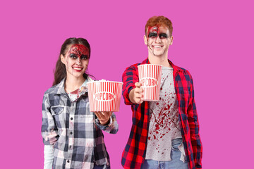 Young couple dressed for Halloween with popcorn on pink background