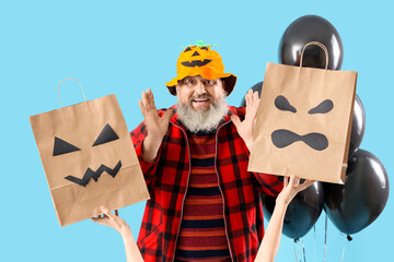 Mature man dressed for Halloween with gift bags and balloons on blue background