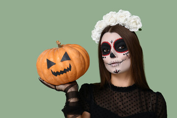 Young woman dressed for Halloween with pumpkin on green background, closeup