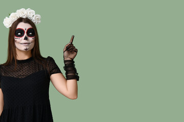 Young woman dressed for Halloween pointing at something on green background