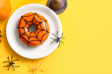 Plate of tasty donut with decorations for Halloween on yellow background