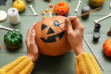 Woman painting Halloween pumpkin at green wooden table