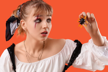 Scared young woman dressed for Halloween with jelly spider on orange background