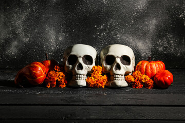 Halloween composition with skulls, pumpkins and marigold flowers on black wooden table