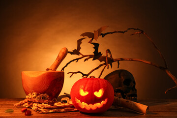 Halloween composition with jack-o-lantern, mortar, pestle and tree branches on wooden table