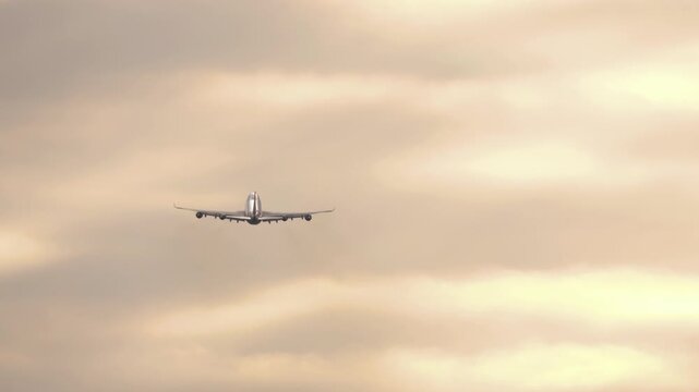 A large four-engine widebody jet aircraft is seen climbing through the sky during a stunning sunset or sunrise. Concepts ir travel and long-haul aviation.