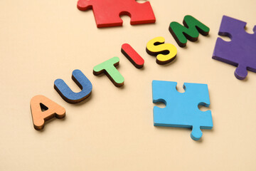 Word AUTISM and colorful puzzle pieces on beige background