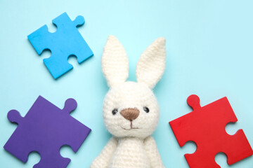 Colorful puzzle pieces and toy bunny on blue background. Concept of autistic disorder. Closeup