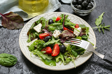 Plate of fresh vegetable salad with feta cheese, tomatoes, olives and arugula on black background